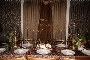 Elegant dark wedding tablescape with green taper candles, ornate plates, floral centerpieces, and a brown fabric backdrop.