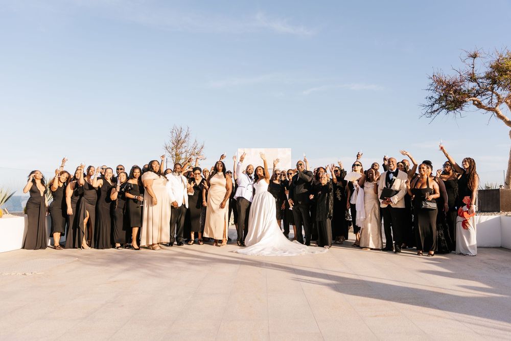 Wedding party celebrating outdoors on a rooftop terrace, bride in white gown surrounded by guests in black and neutral attire.