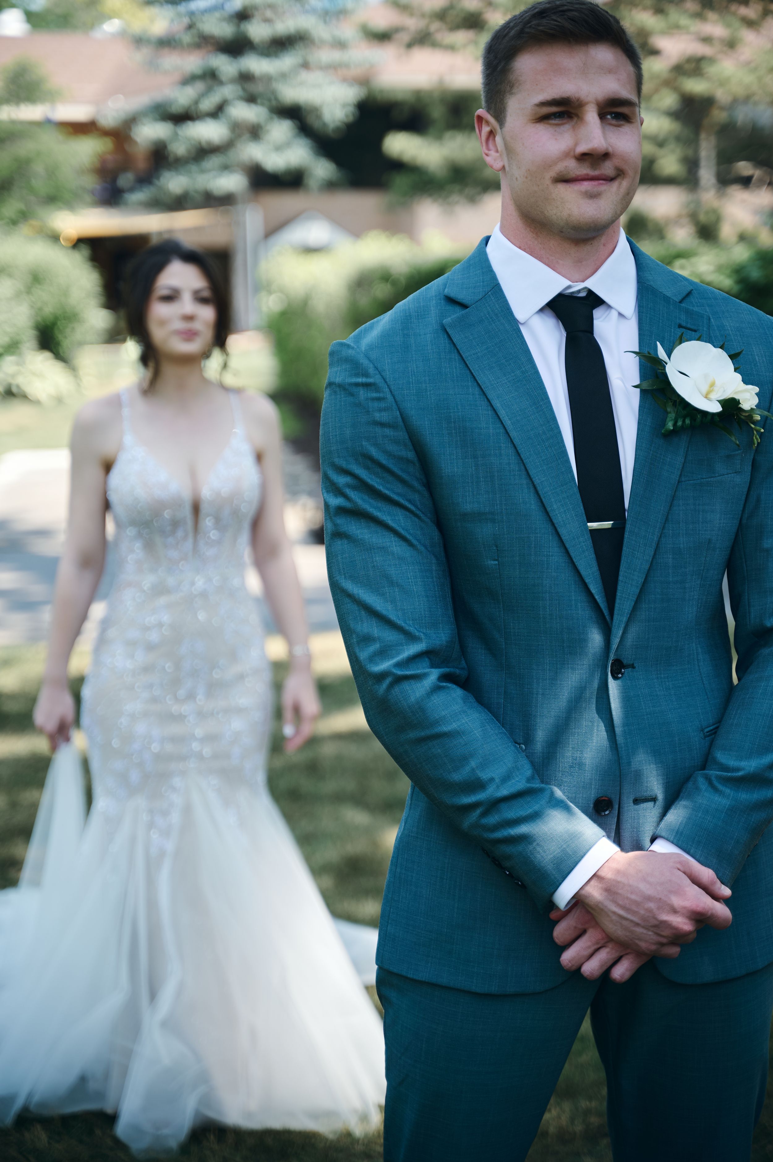 Groom in teal suit with white boutonniere awaits bride in beaded gown for first look.