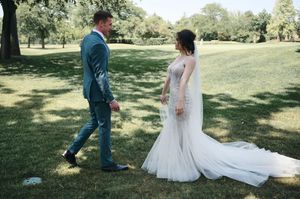 Bride and groom holding hands walking in a green park, groom in teal suit, bride in elegant fitted wedding dress.