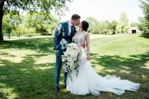 Newlyweds share a kiss outdoors, bride holding white floral bouquet in mermaid gown.