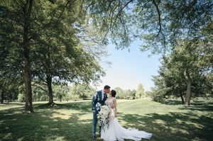 Bride and groom share a romantic kiss surrounded by lush green trees on their wedding day.