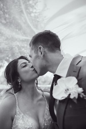 Black and white photo of bride and groom sharing a romantic kiss under flowing wedding veil.