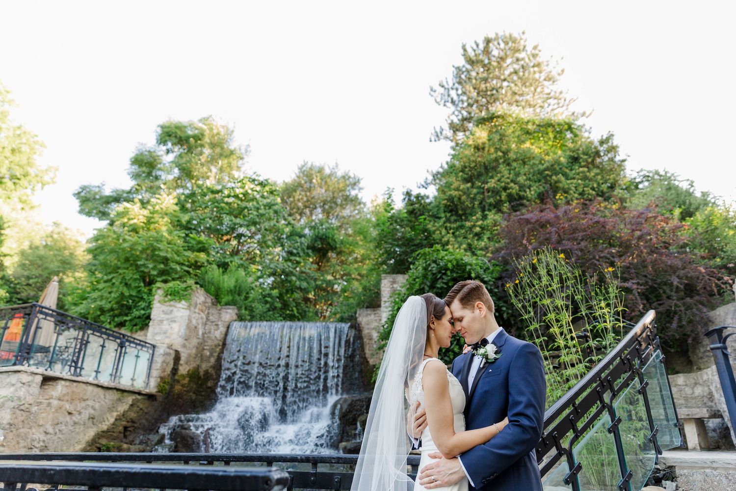 Relaxed wedding photography of bride and groom snuggling into each other in front of the waterfall at the ancaster mill in ancaster, ontario