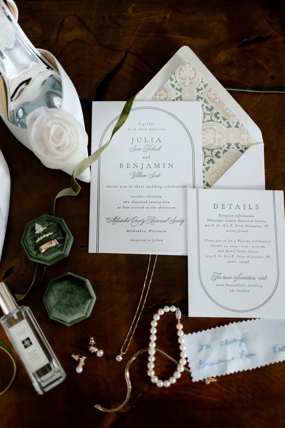 Elegant wedding invitation suite with pearl bracelet, earrings, rings in velvet box, and Jo Malone perfume on dark wood.