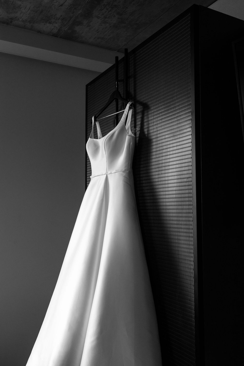 Elegant white wedding dress hanging on a wooden cabinet in a black and white photo.