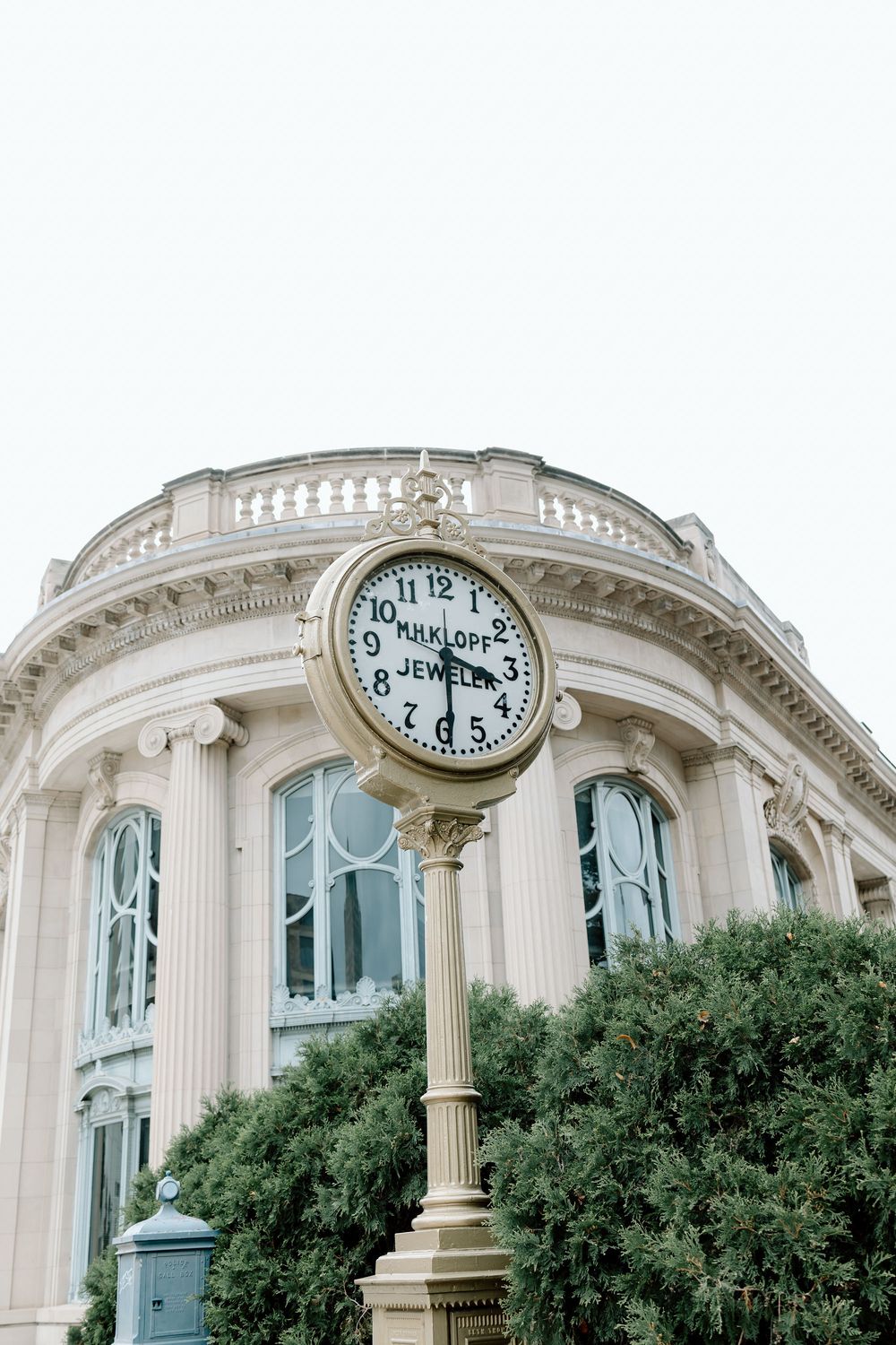 Ornate beige building facade with decorative columns behind a vintage Kirklof Jewelers street clock on a pole.