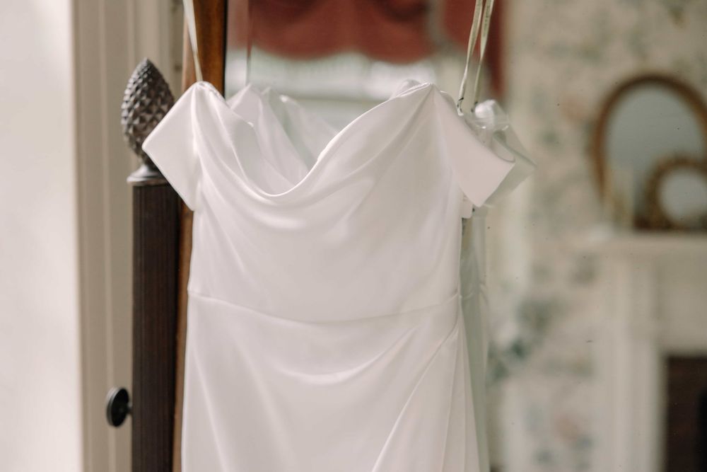 Close-up of a white off-shoulder wedding dress with draped neckline on a hanger.