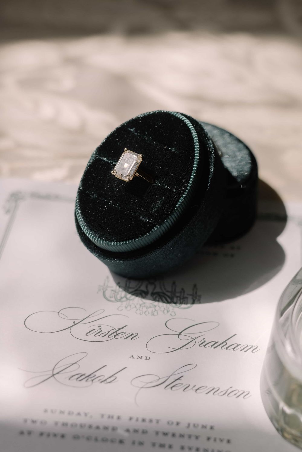 Emerald cut diamond engagement ring in a green velvet box on a wedding invitation.