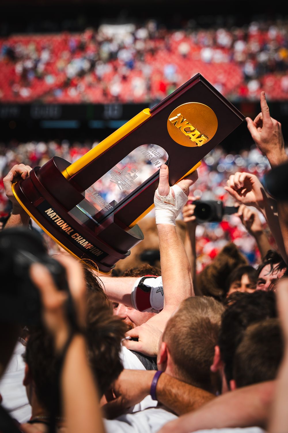 Crowd celebrates as NCAA National Championship trophy is raised high in a packed stadium.