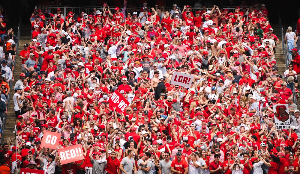 Large crowd of fans in red jerseys filling stadium bleachers, holding signs including GO REAL at a sports event.