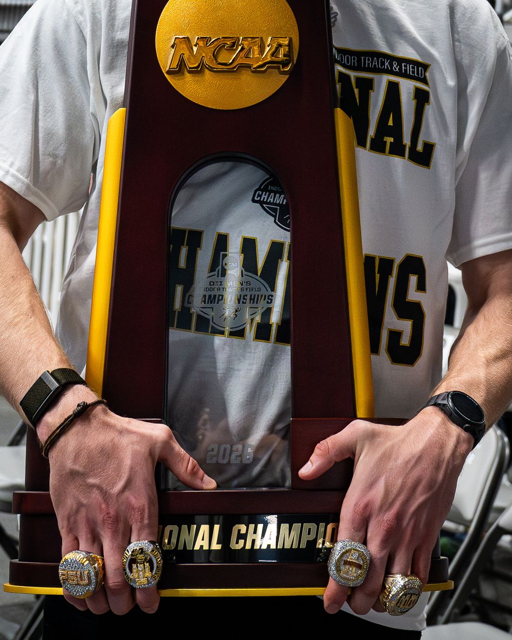 Person holding NCAA National Championship trophy wearing championship rings, celebrating a track and field title win.