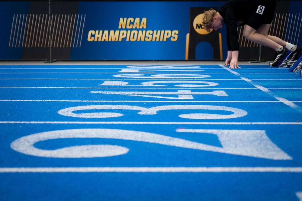 Athlete in starting position on blue NCAA Championships indoor track with lane numbers visible.