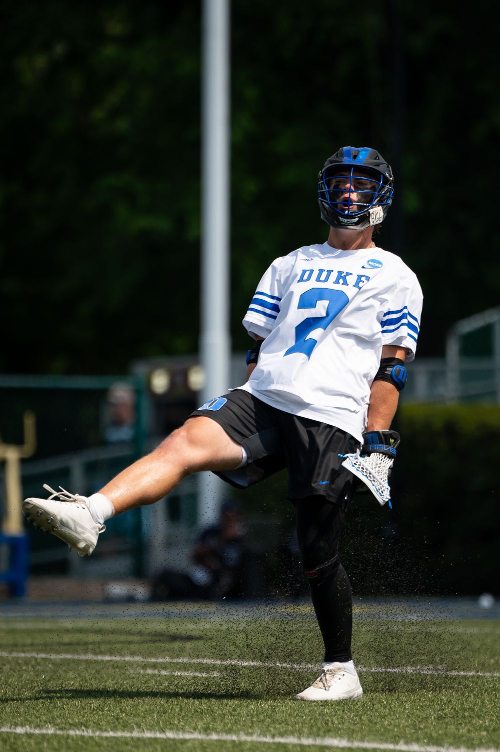 Duke lacrosse player #2 in white uniform mid-action on turf field wearing blue helmet during sunny game.