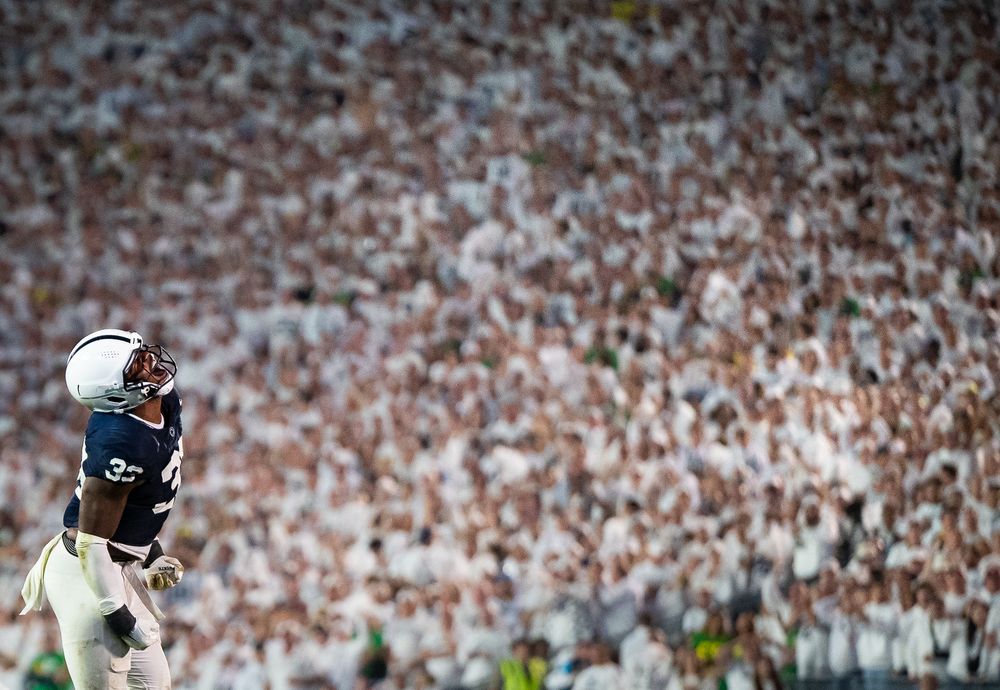 Penn State football player stands on field before a packed stadium of fans dressed in white during a game.