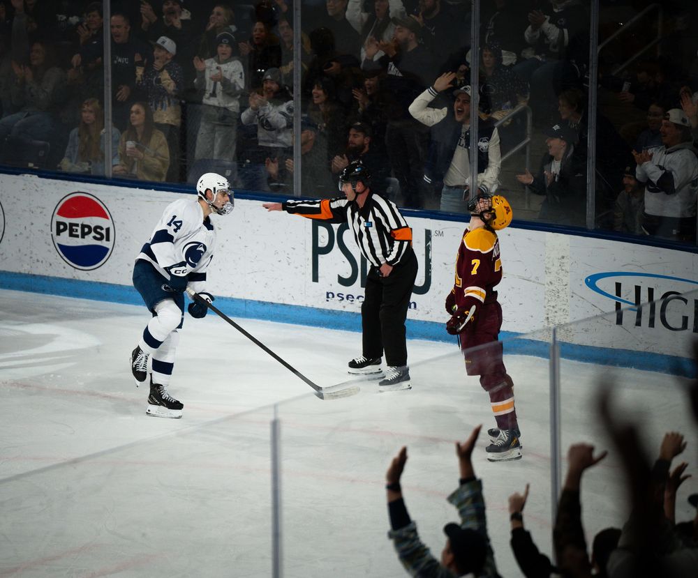 Hockey players face off during a game with a referee and fans visible in the background near a Pepsi advertisement.