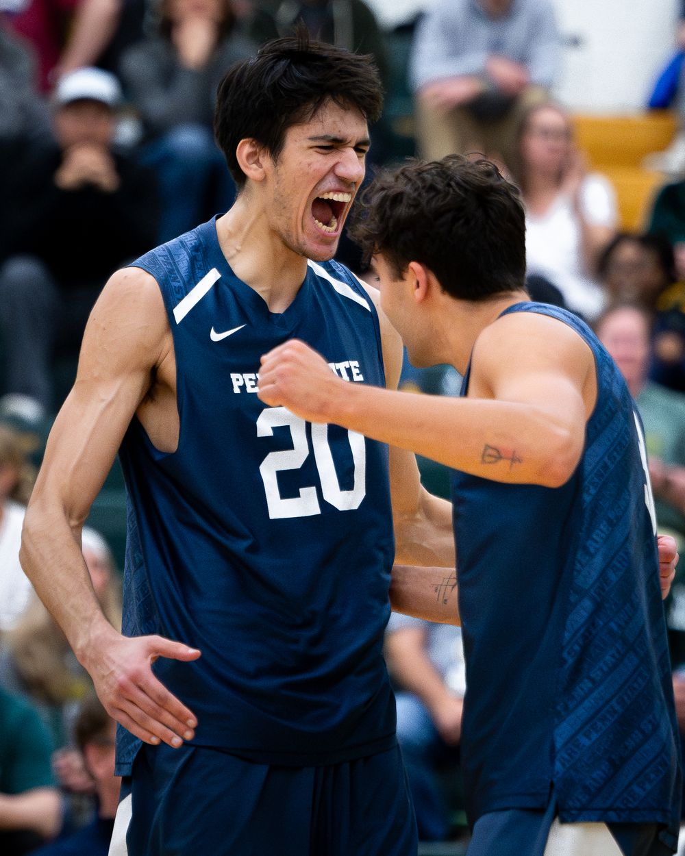 Two Penn State volleyball players celebrate intensely during a match wearing navy uniforms.