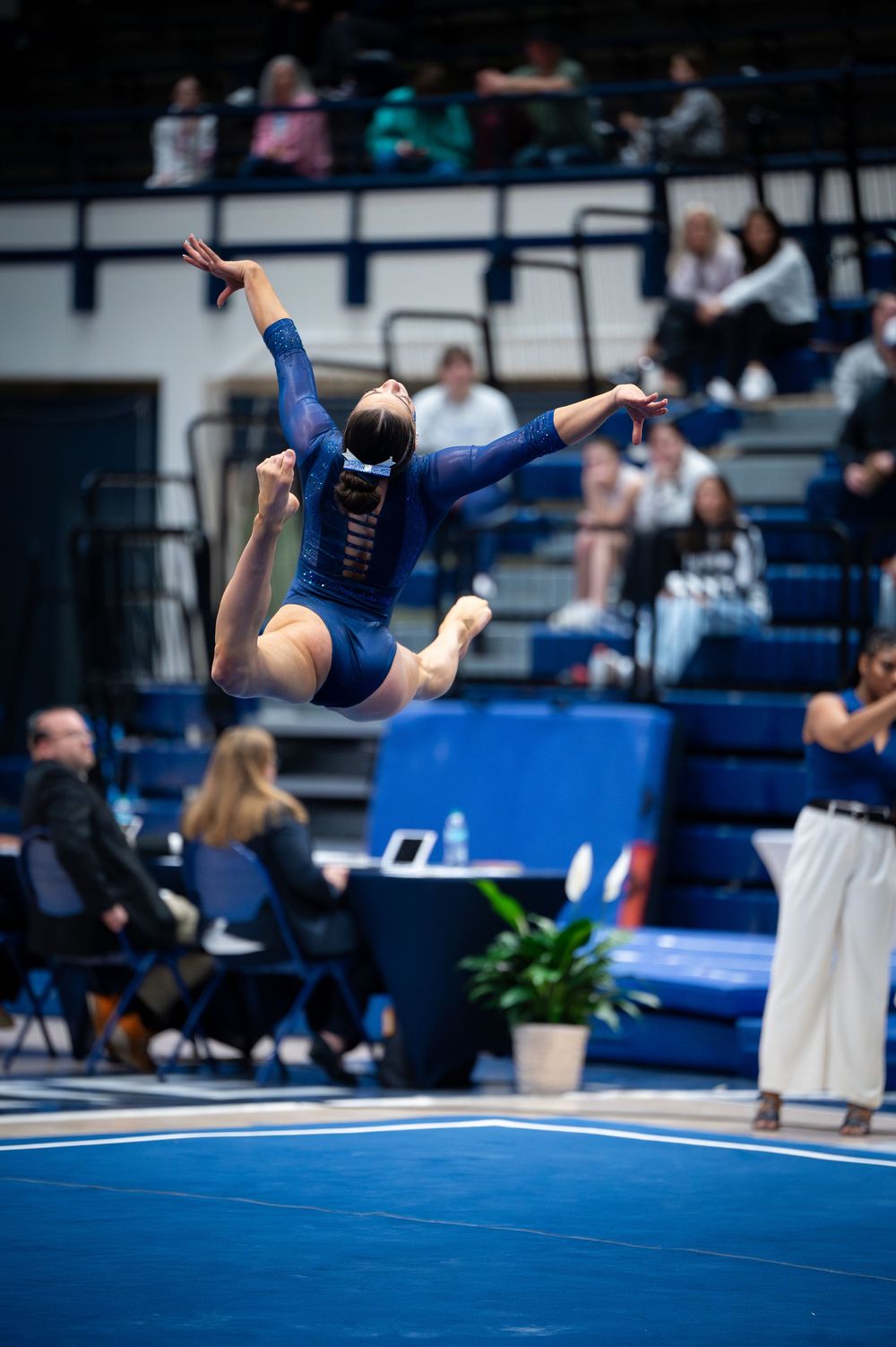 A gymnast performs a dynamic back flip during a floor exercise routine on blue competition mats.