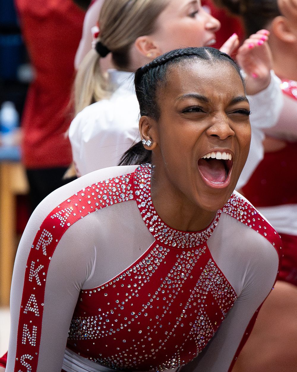 An athlete in a sparkly red and white leotard shows pure joy and excitement while celebrating during competition.