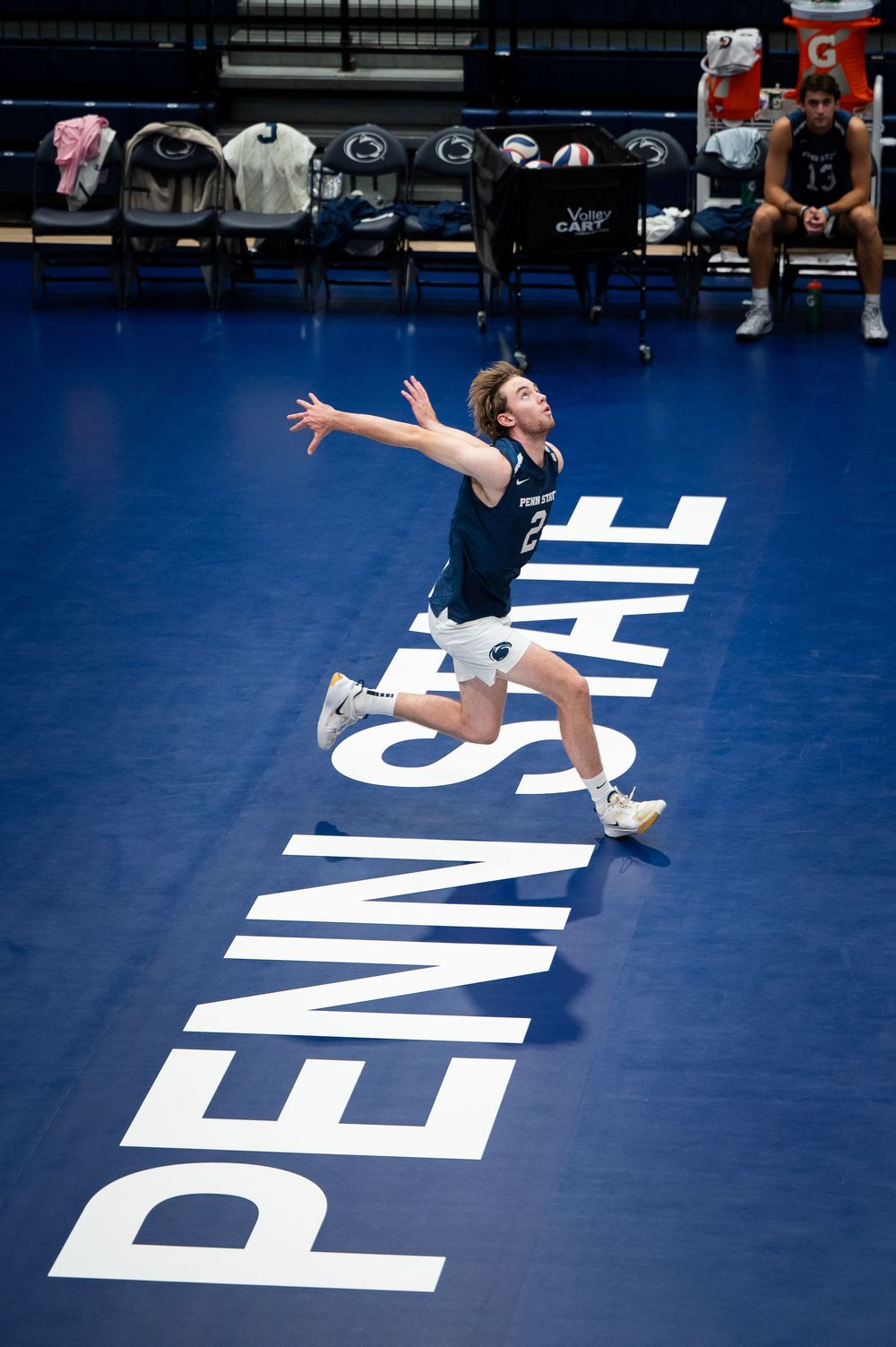 A gymnast performs a dynamic aerial split leap sequence on a blue competition floor with white text markings.