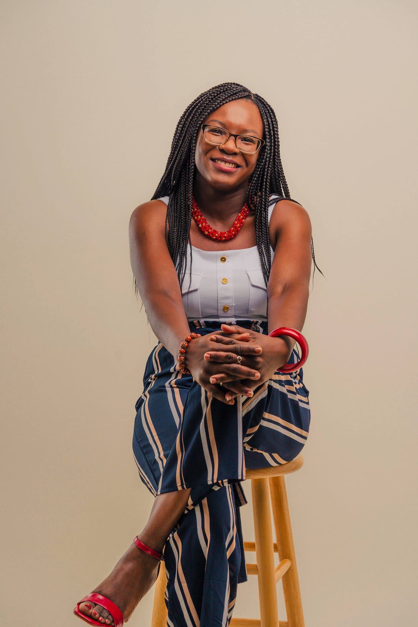 Casual studio portrait featuring braided hair, red necklace and striped pants.