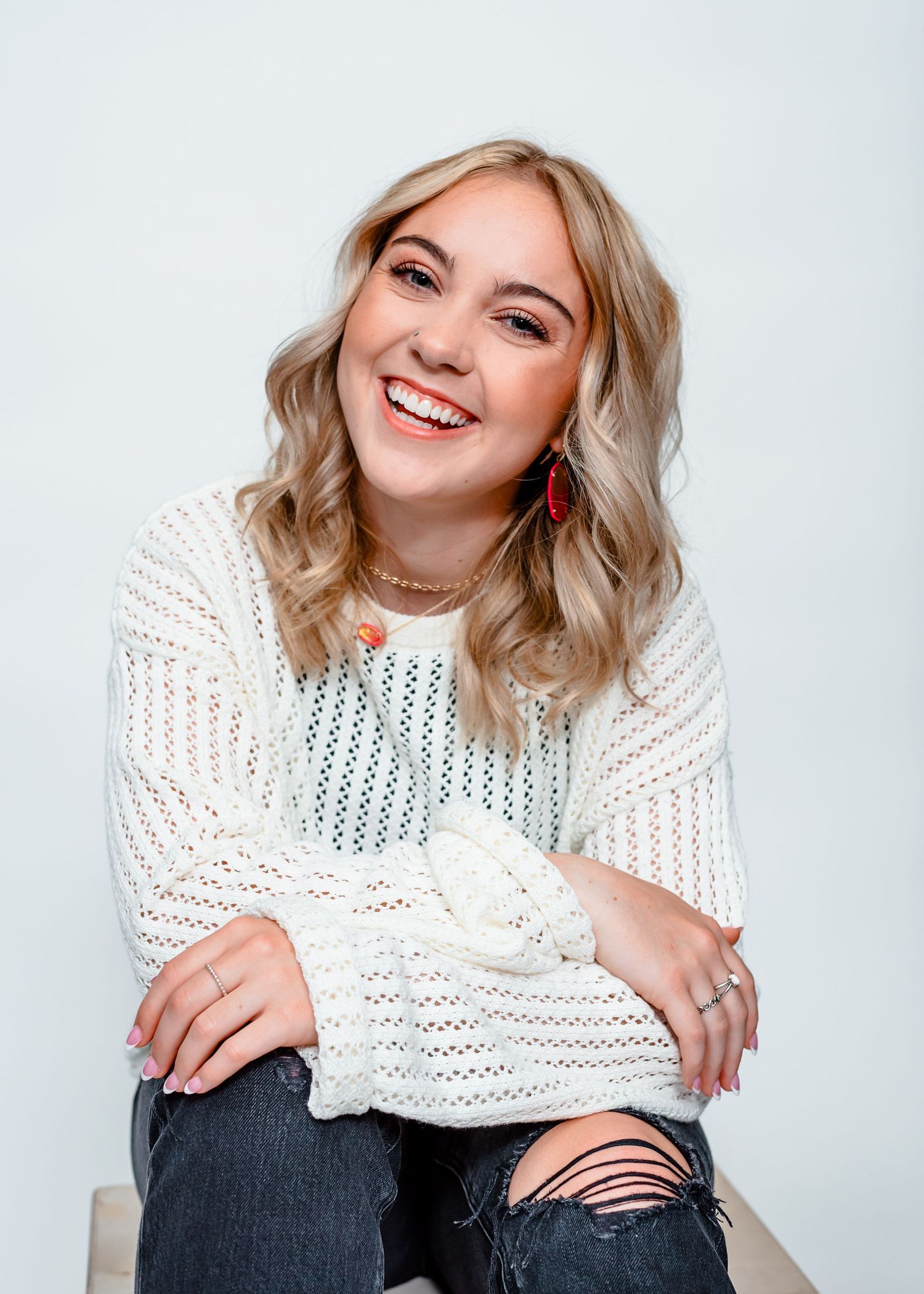 Portrait of woman in white knit sweater and ripped jeans smiling at camera.