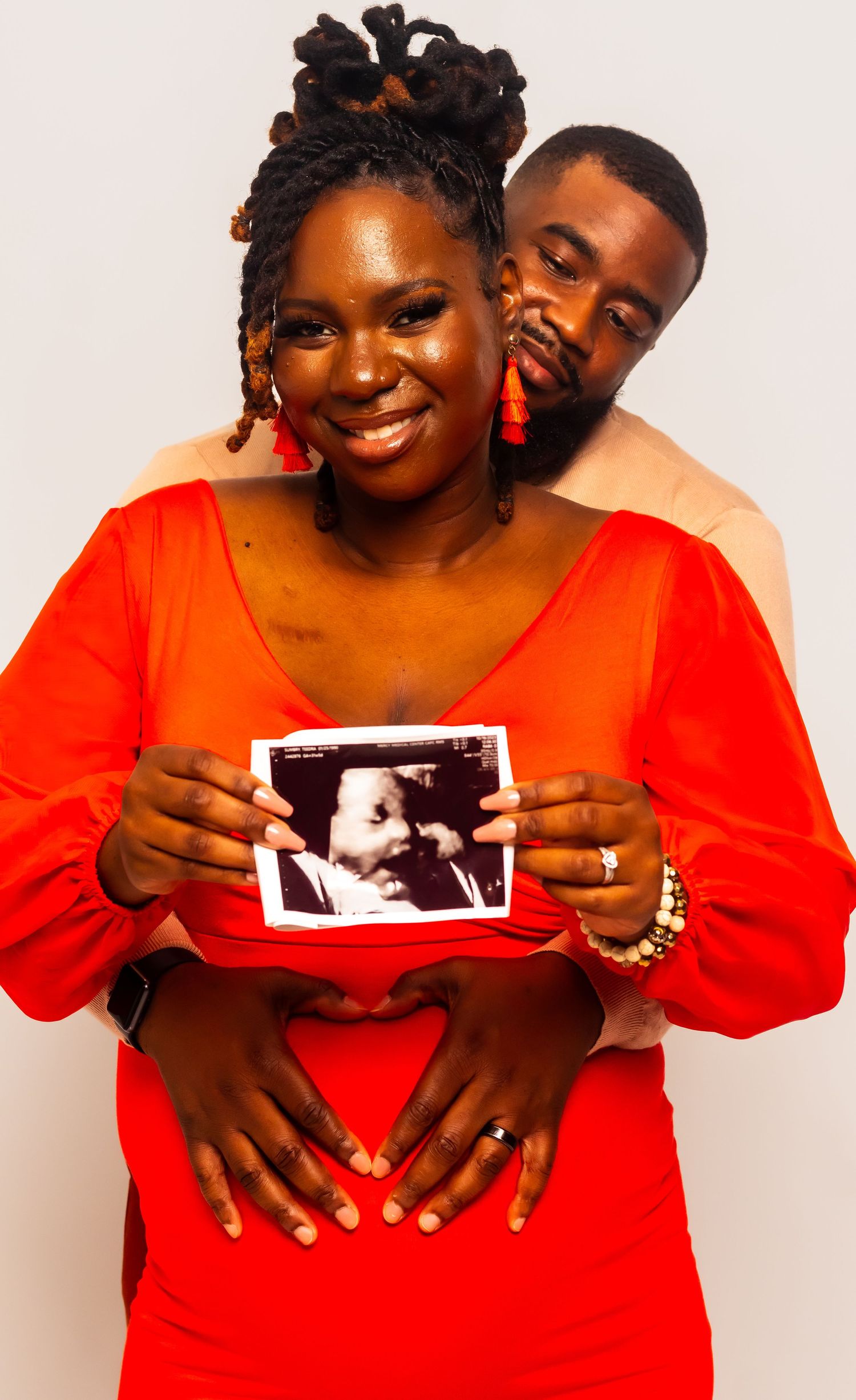 A maternity photo session featuring a couple in red holding an ultrasound photo.