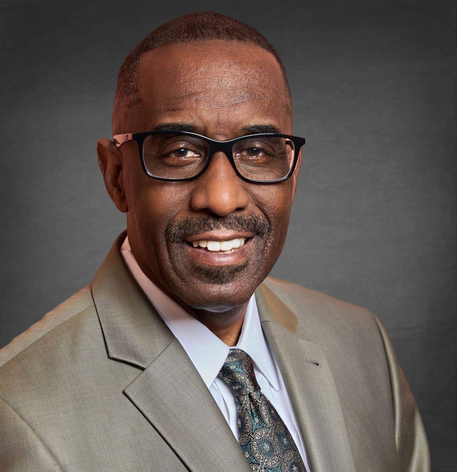 Professional headshot series in tan suit with patterned tie against grey background.