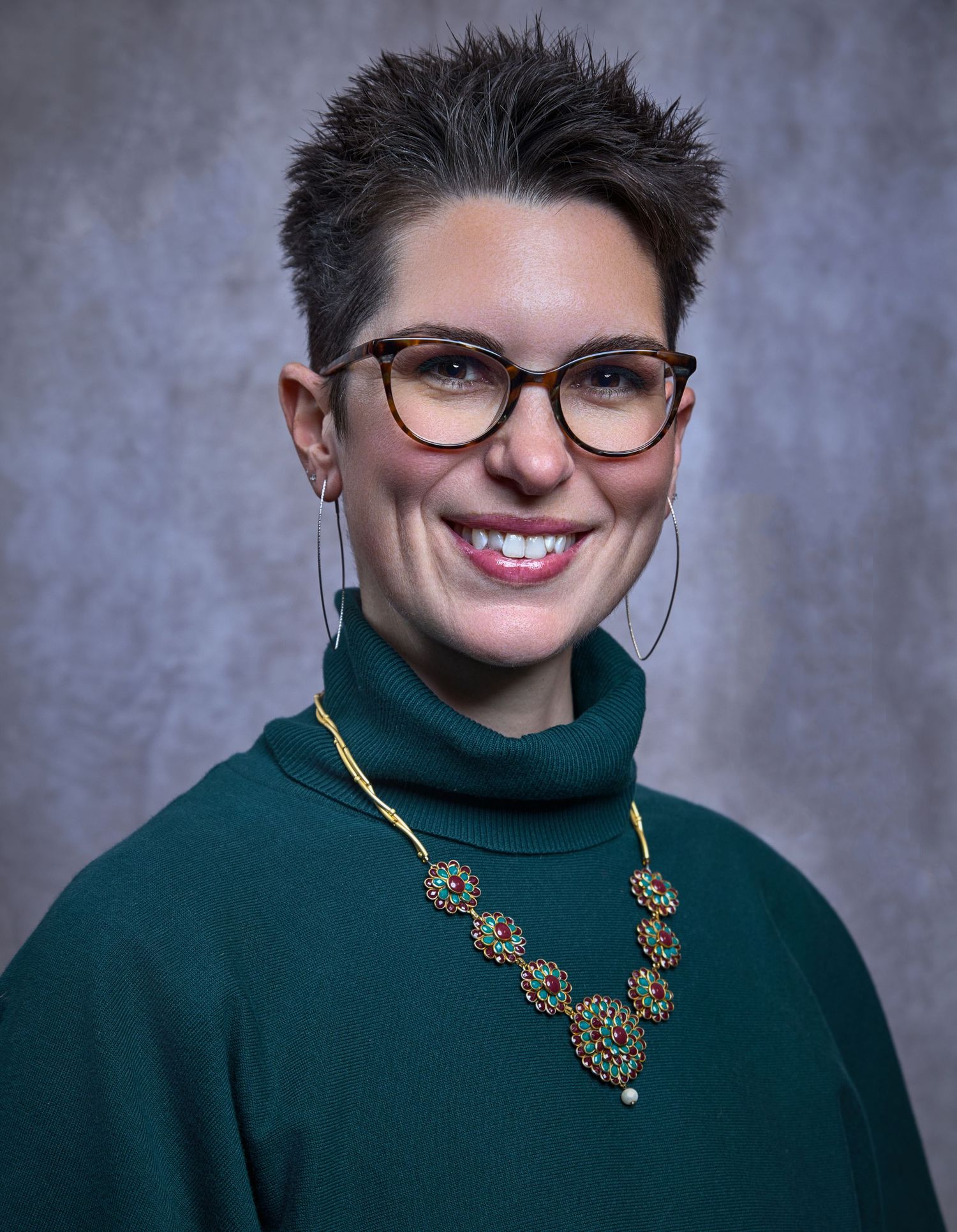 Professional headshot series showing person in dark green turtleneck and statement necklace against gray background.