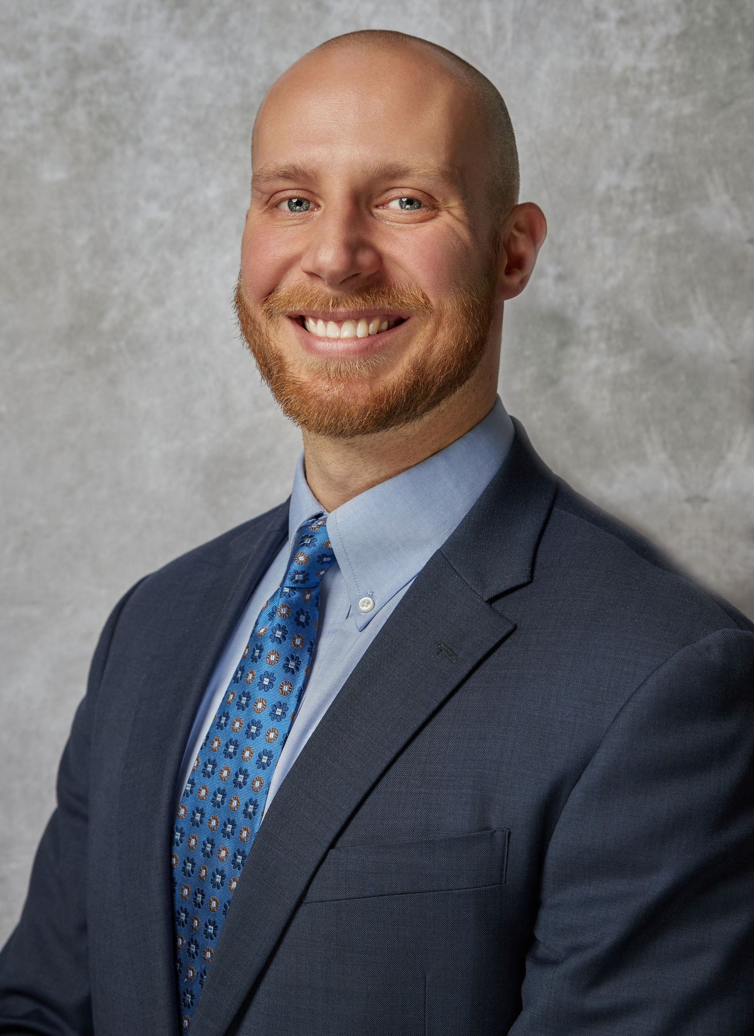 Professional headshot series showing person in navy suit with blue patterned tie against gray background.