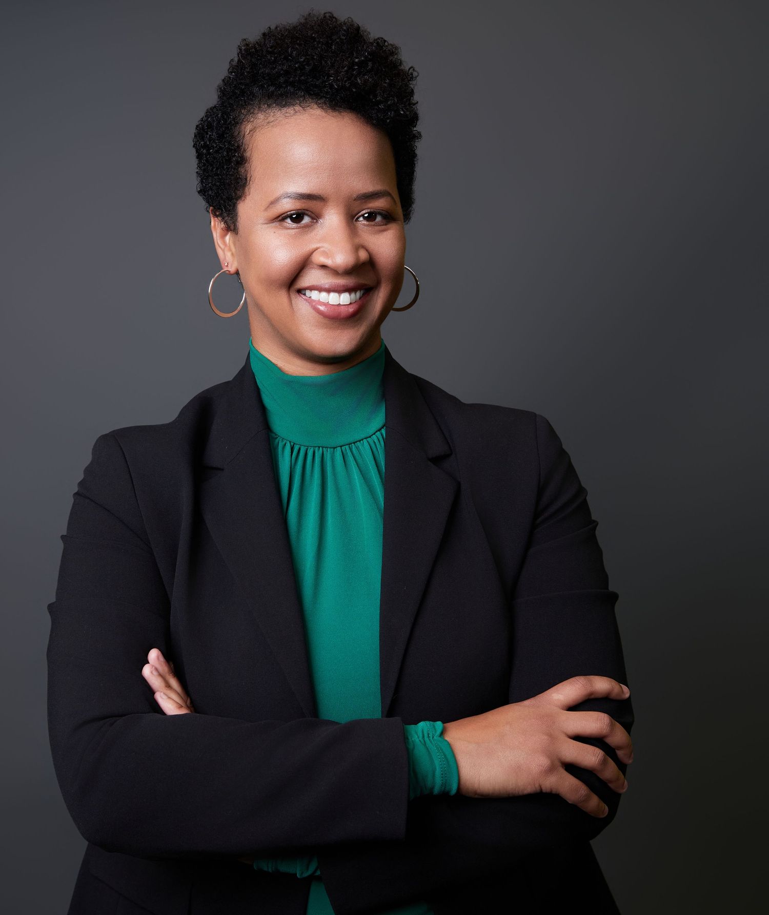 Professional portrait series in black blazer and emerald green top against dark background.
