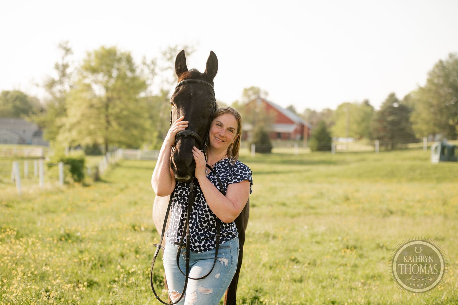 A woman in a patterned top shares a tender moment with her horse in a grassy field at sunset.