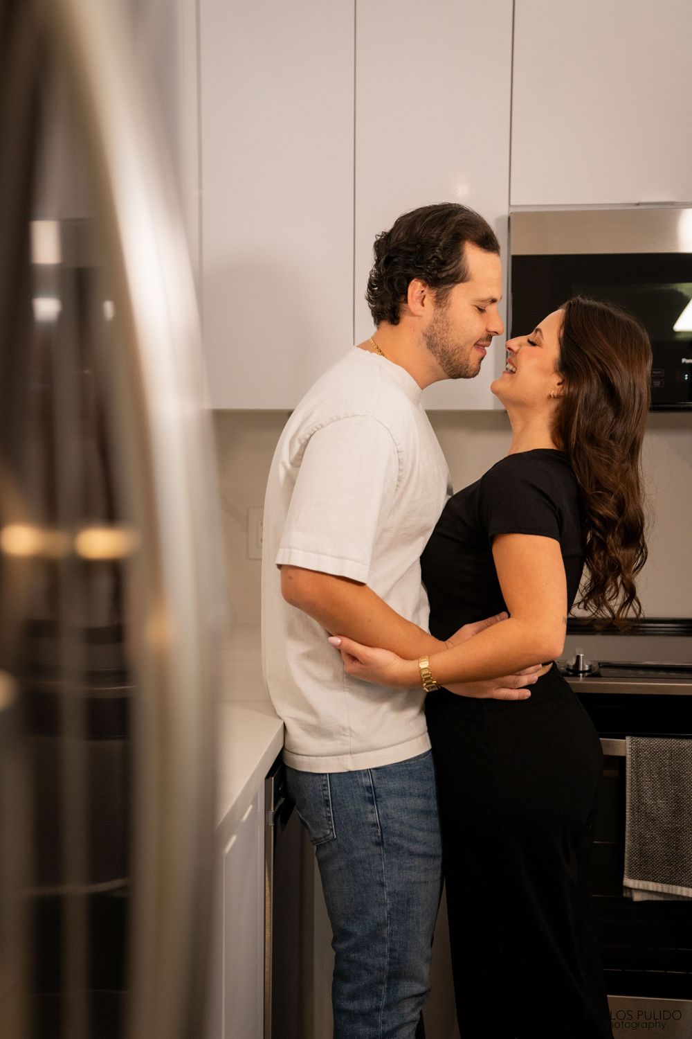 A romantic couple embracing in a modern kitchen with soft lighting.