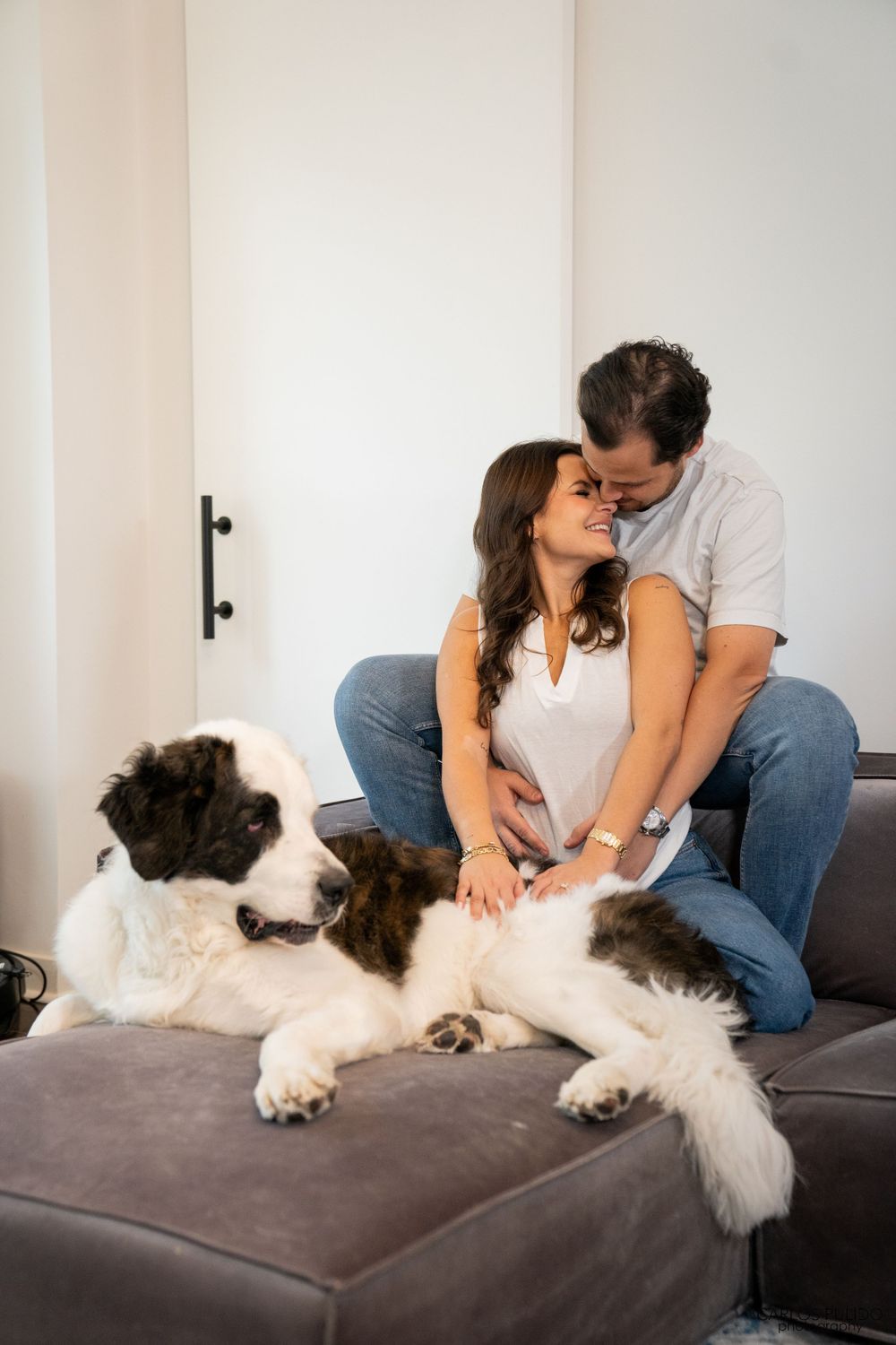 A couple cuddling on a couch with their large black and white dog.
