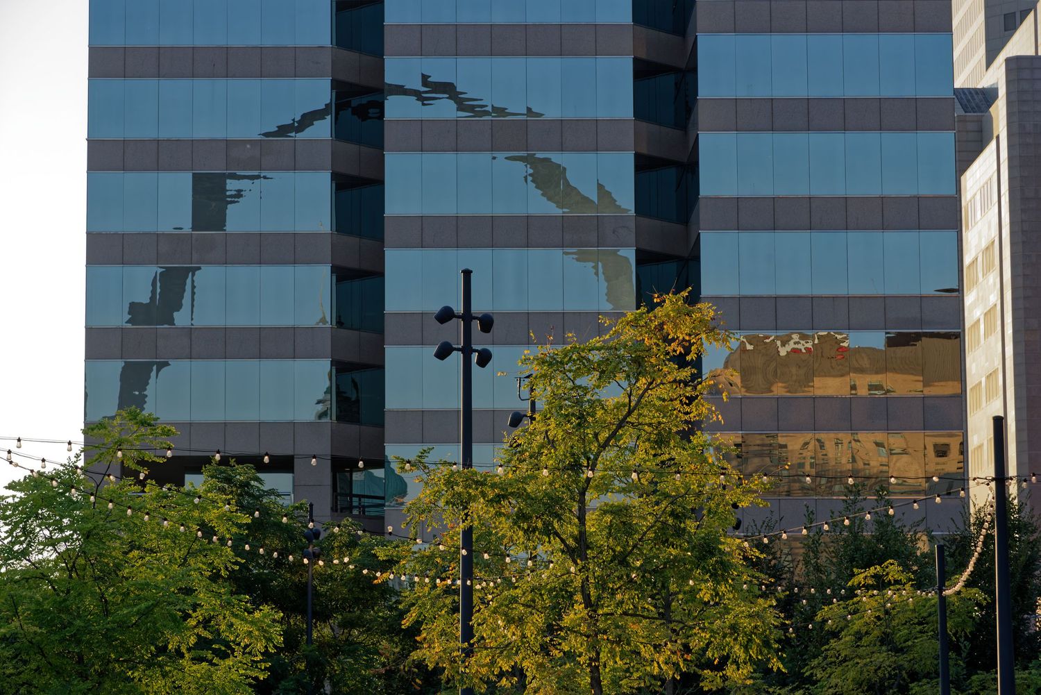 Glass office building reflects sky and clouds with autumn trees in the foreground.