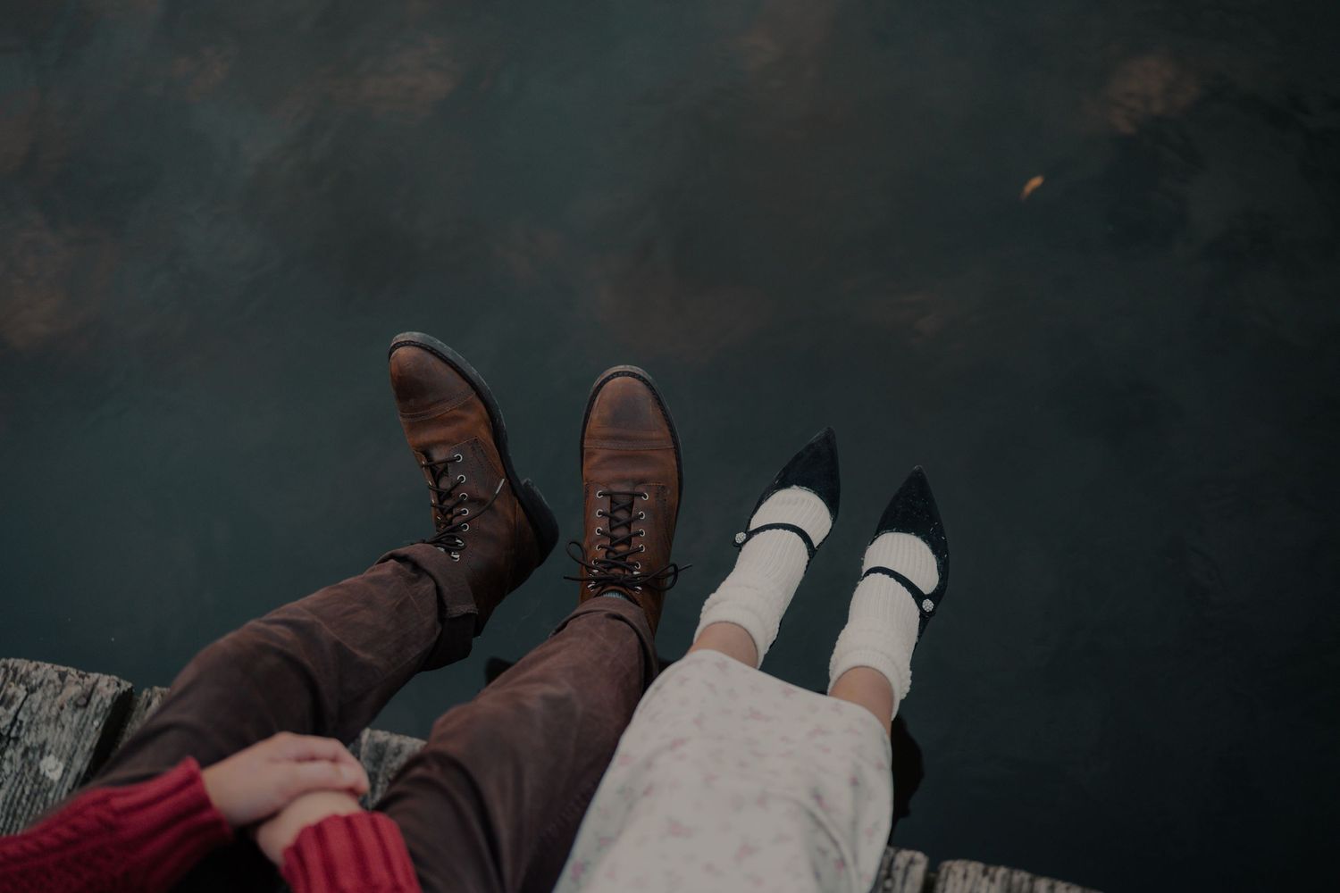 Two pairs of feet dangling over an edge, one wearing brown boots and the other white shoes.