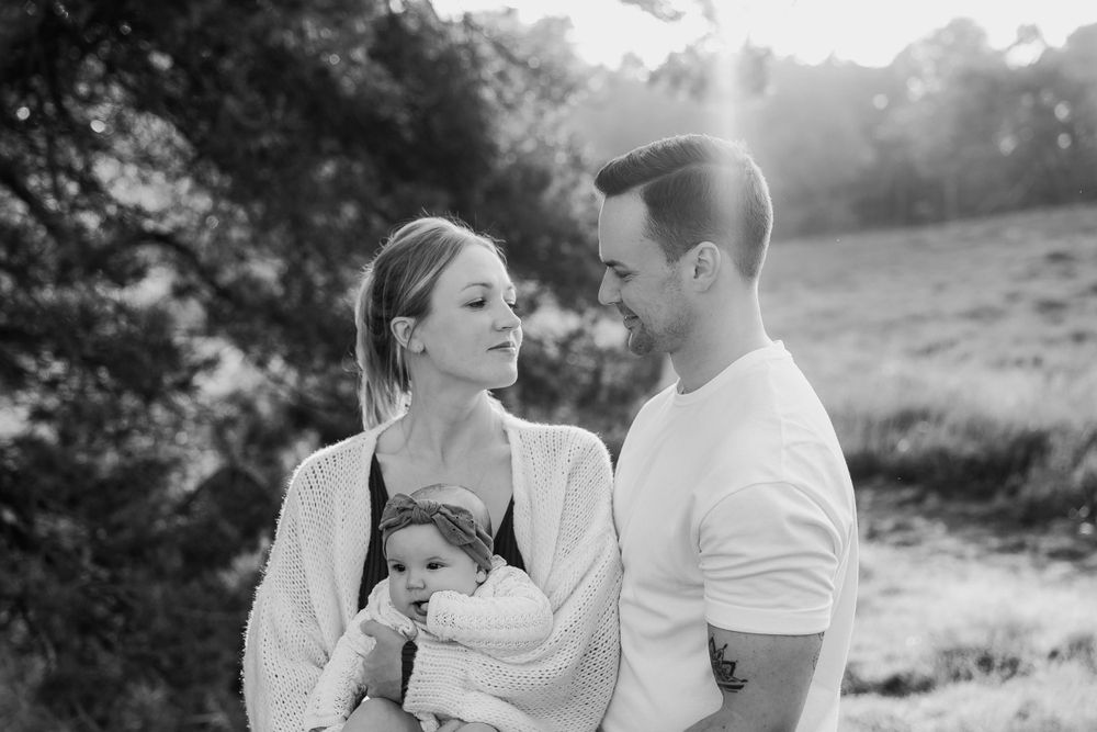 A tender family moment captured in black and white as they gather outdoors in a natural setting.