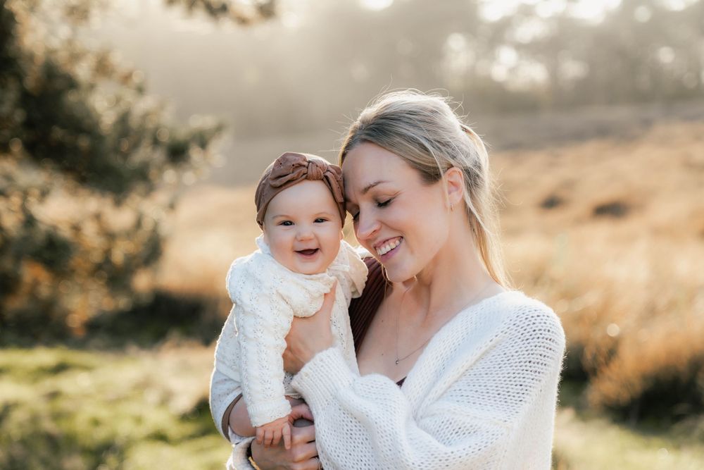 A joyful portrait of parent and baby against a warm sunlit natural background.