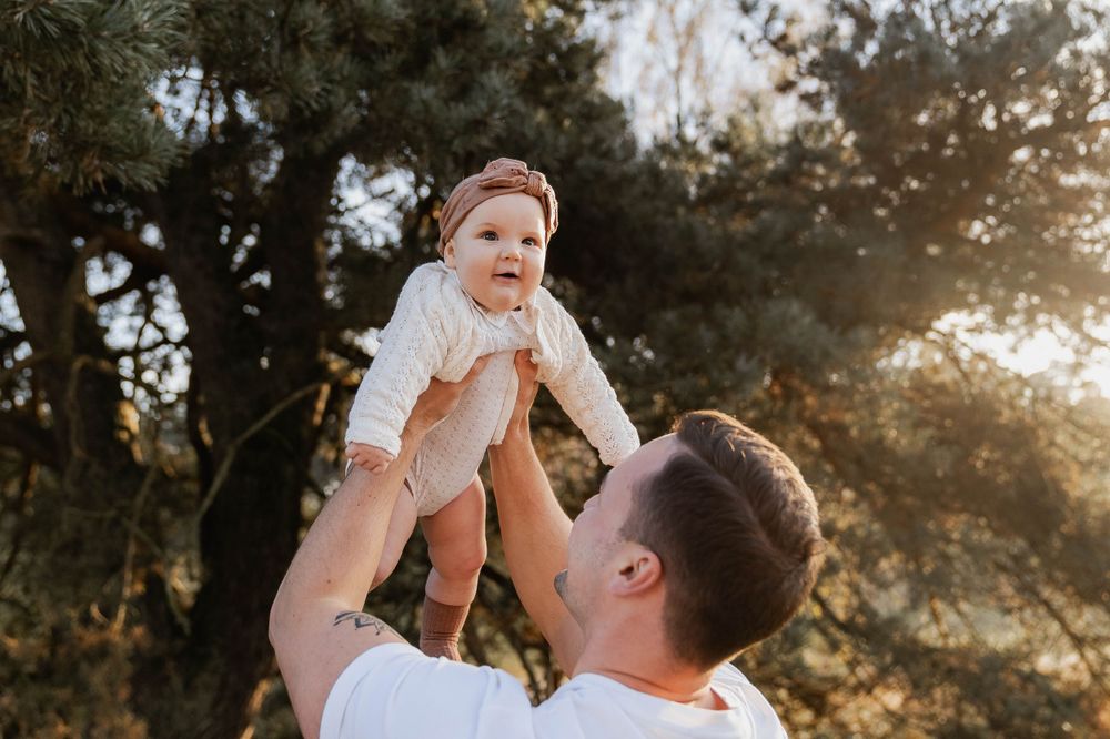 A playful moment between parent and baby lifted against the setting sun.