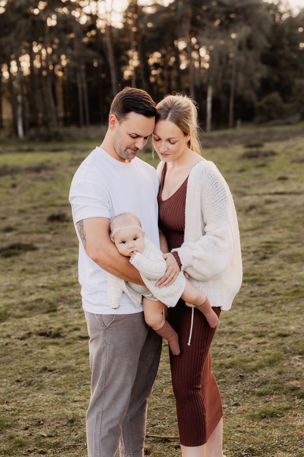 A sweet family portrait in casual attire standing together in an open field at sunset.
