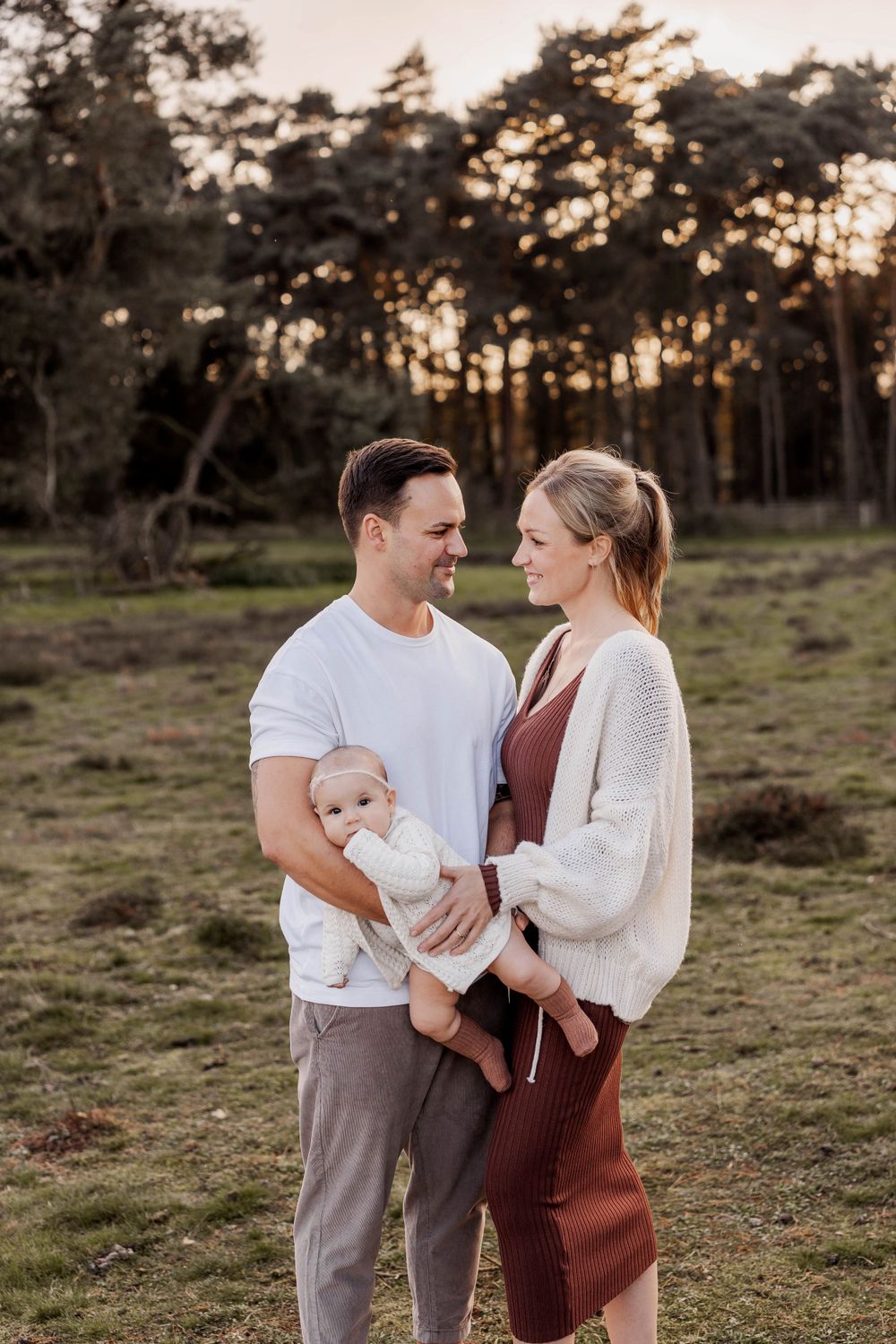 A young family shares an intimate moment at sunset in a wooded field.