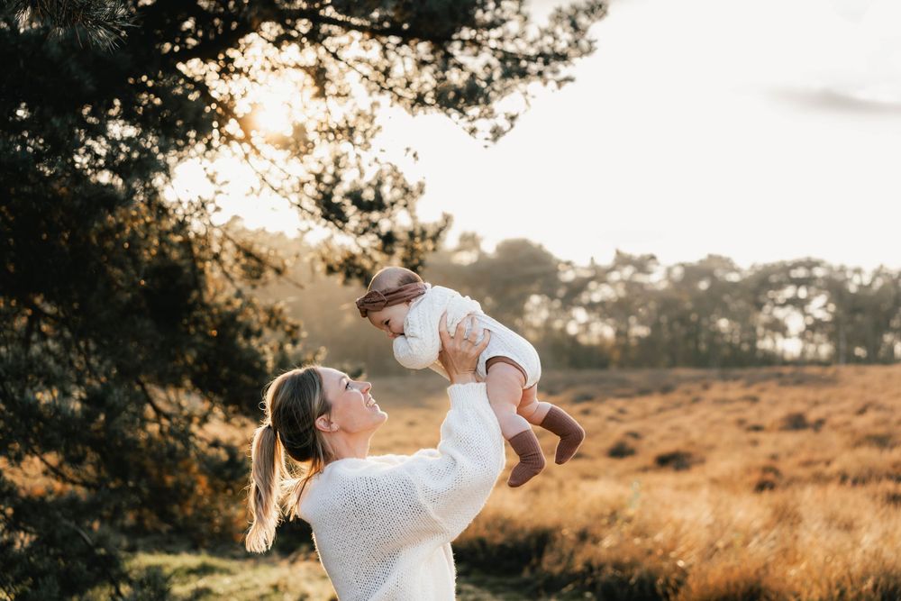 Parent lifting baby in the air during golden hour in nature setting.