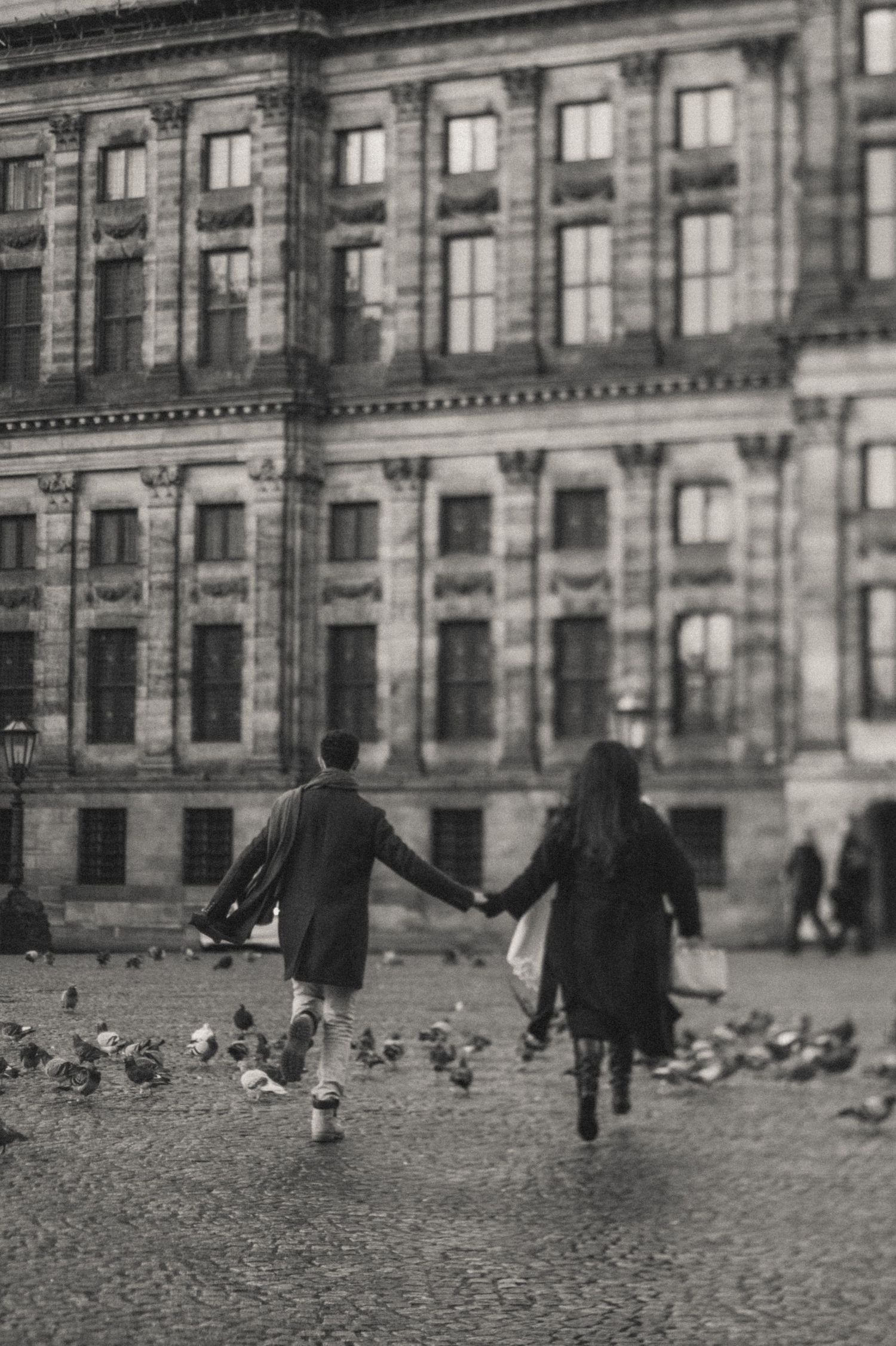 People walking across a cobblestone plaza in front of a historic European building.