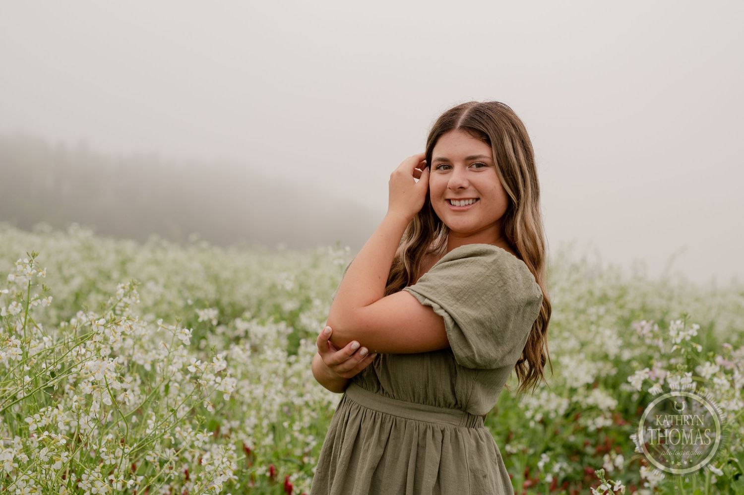 A misty outdoor portrait with someone in a casual green dress posing in a flowering meadow.