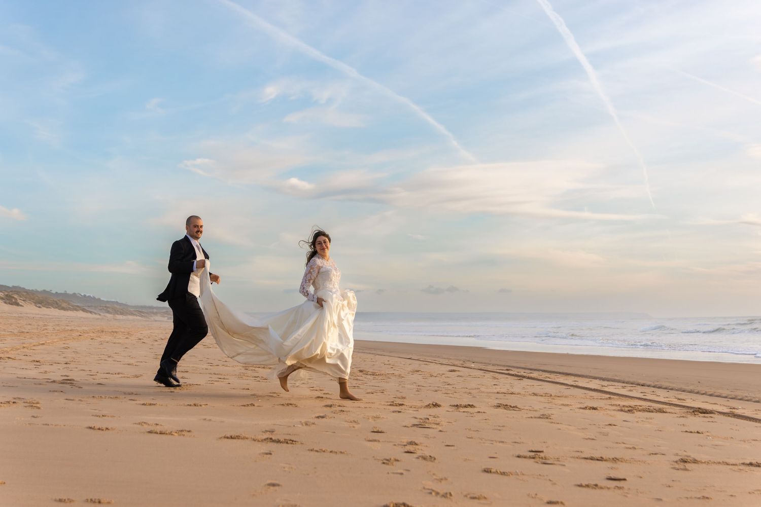 Silhouettes of people on a beach with seabirds flying overhead at sunset.