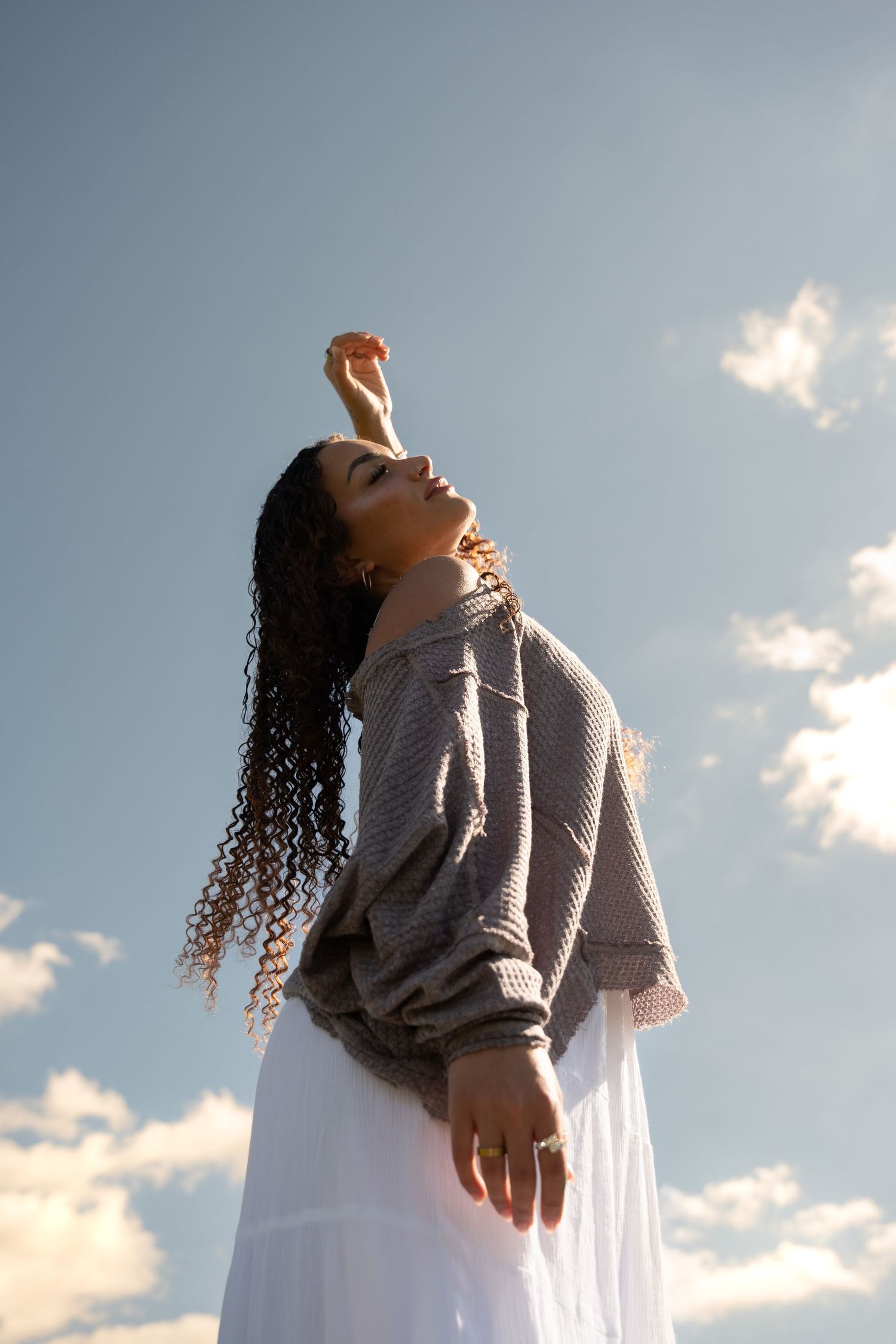 Girl with her head in the clouds, face tilted toward the sun, hair flowing in the summer breeze, capturing a dreamy and carefree vibe.