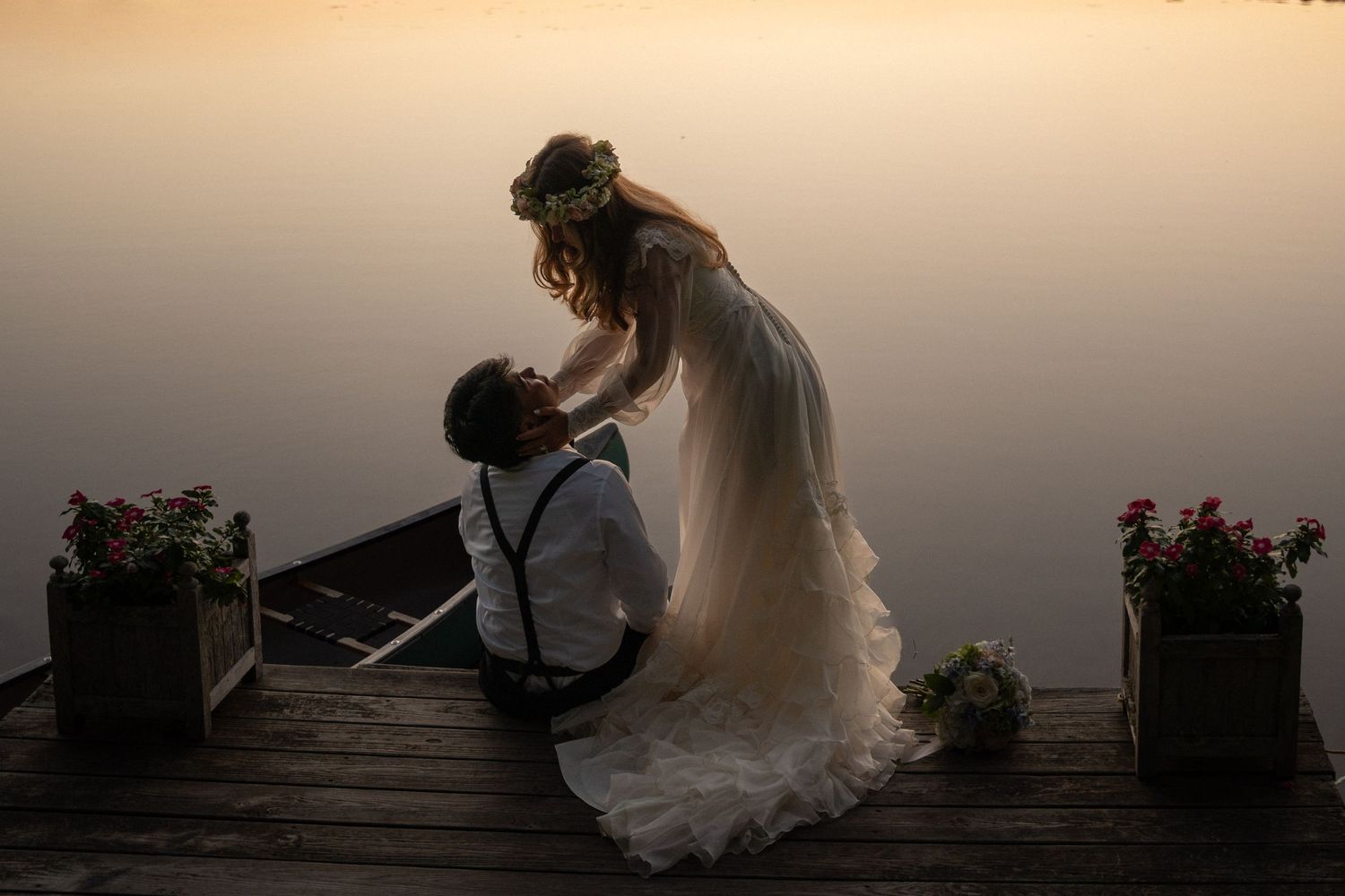 Couple on a dock at sunset on their wedding day, sharing a quiet, intimate moment with warm golden light reflecting off the water.