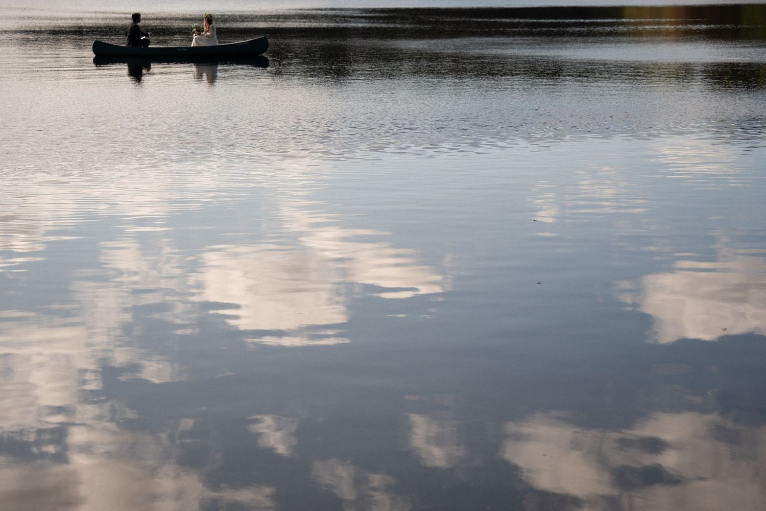 Newlywed couple on a boat ride, surrounded by serene waters with a perfect reflection of clouds, on Cape Cod.
