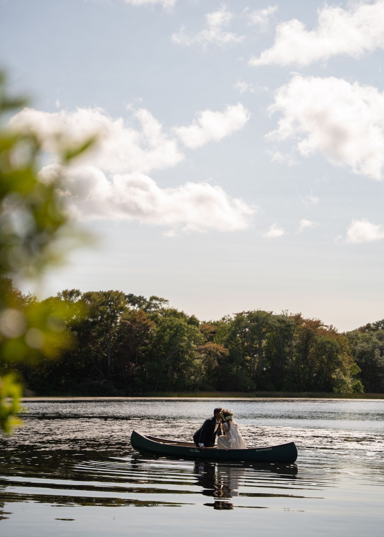 Wedding couple in a canoe on a serene Cape Cod lake, surrounded by peaceful water and lush greenery, creating a romantic and timeless scene