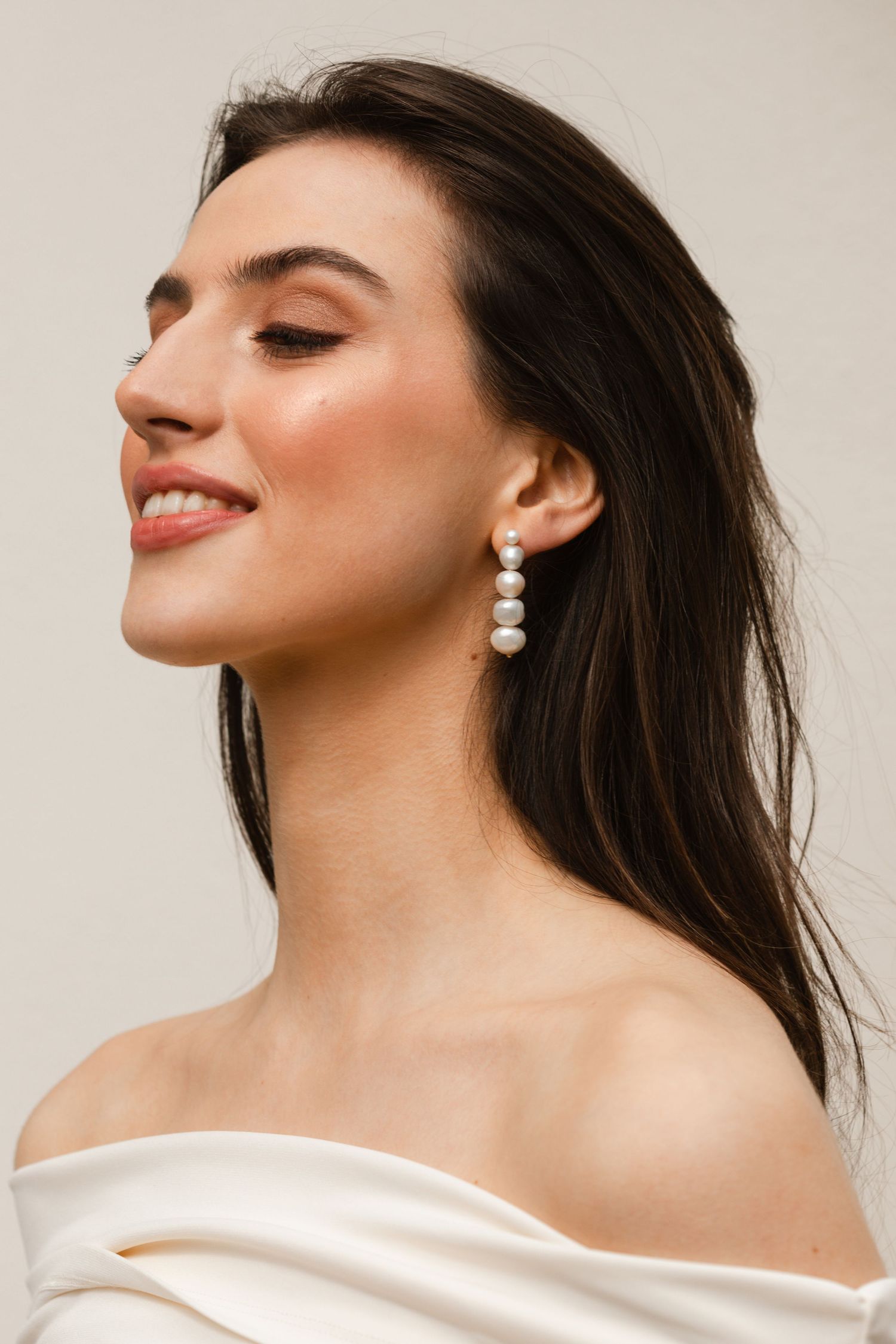 Soft beauty portrait featuring pearl drop earrings and an off-shoulder white top with natural makeup look.